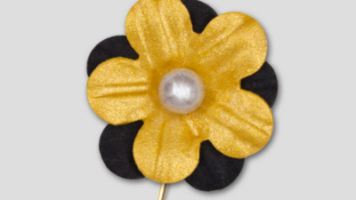 En pappersblomma på en nål. Blomman är guldig med svarta blad runt.