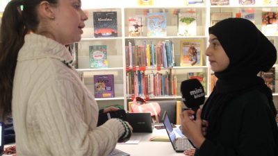 En elev på reporterskolan intervjuar koncentrerat sin lärare och håller i en mick som det står Minibladet på.